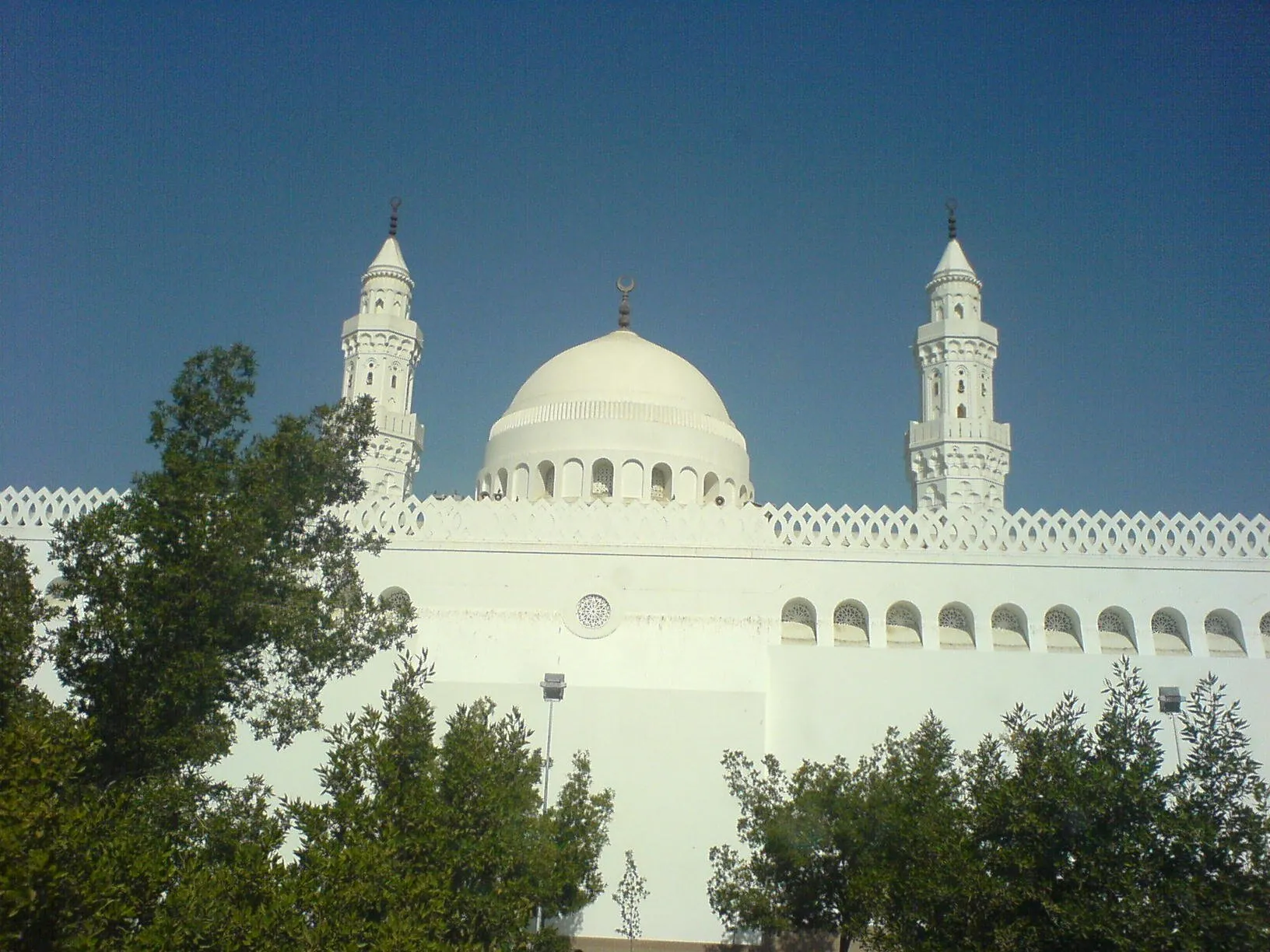 Cúpula branca e dois minaretes da Mesquita de Qiblatain, com árvores em primeiro plano.