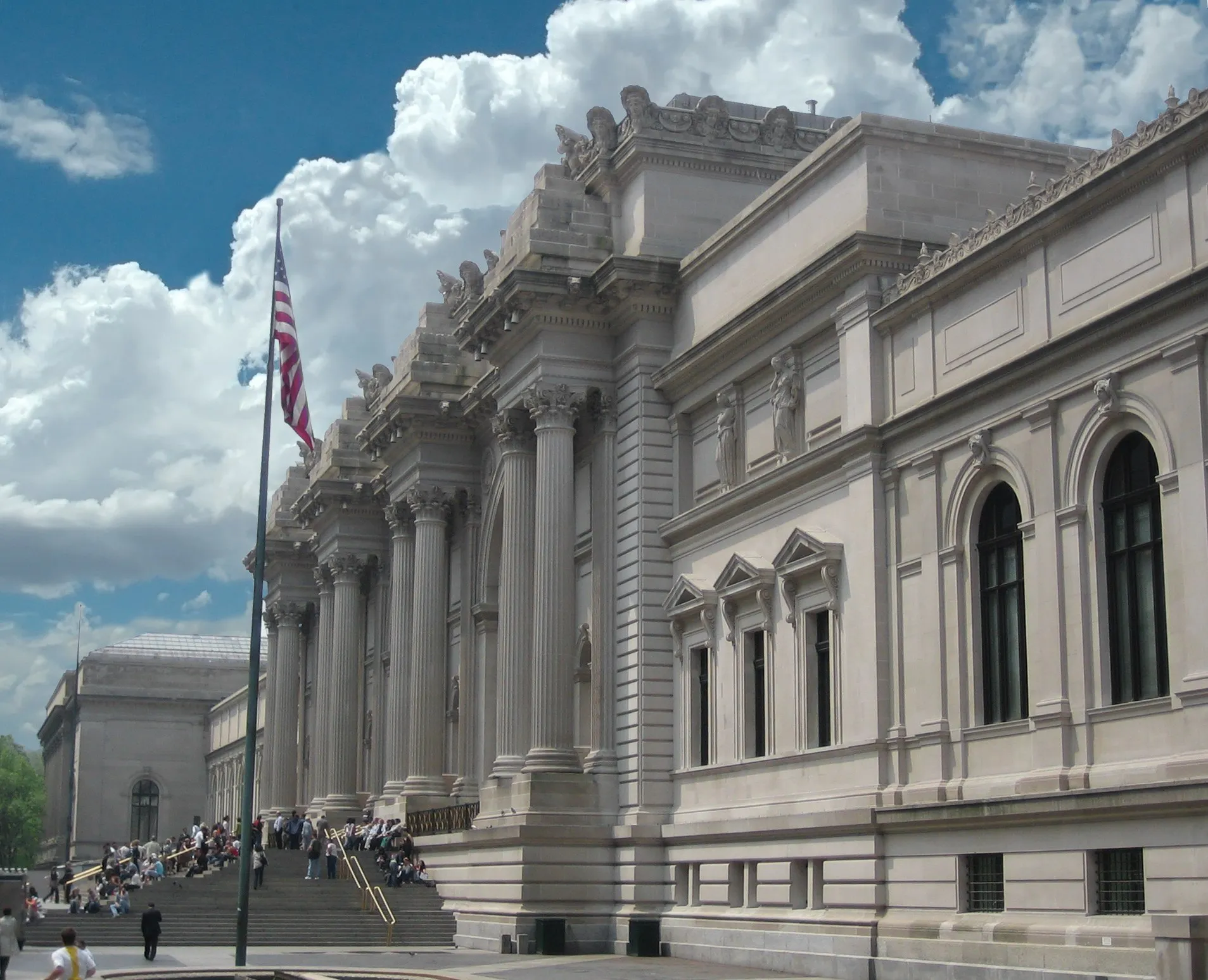 Fachada neoclássica do Metropolitan Museum, na Quinta Avenida, com colunas altas, bandeira e escadaria sob céu azul.