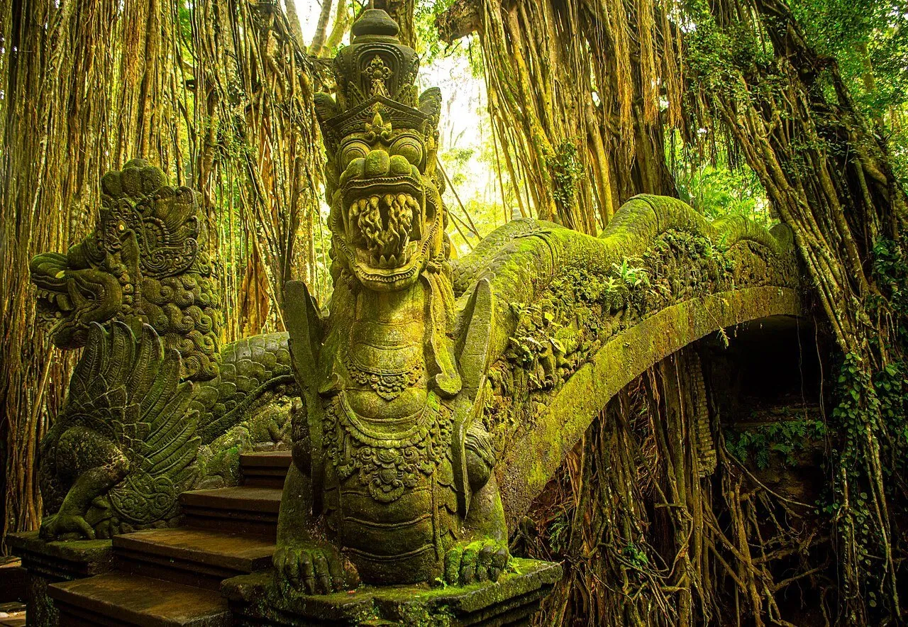 Puente de piedra con esculturas de dragones y musgo, rodeado de raíces colgantes en el Bosque de los Monos de Ubud.