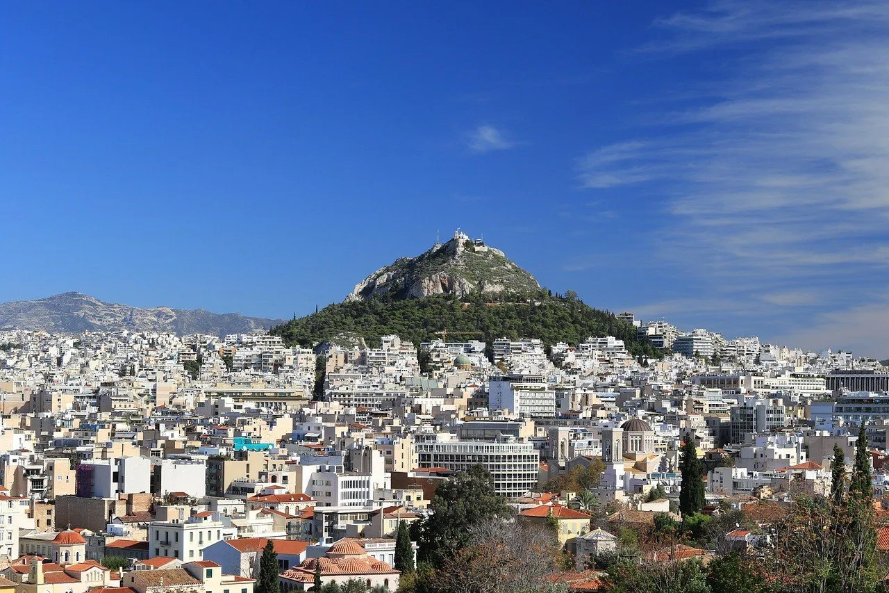 Mount Lycabettus with a white chapel at the summit, slope vegetation and Athens buildings in front.