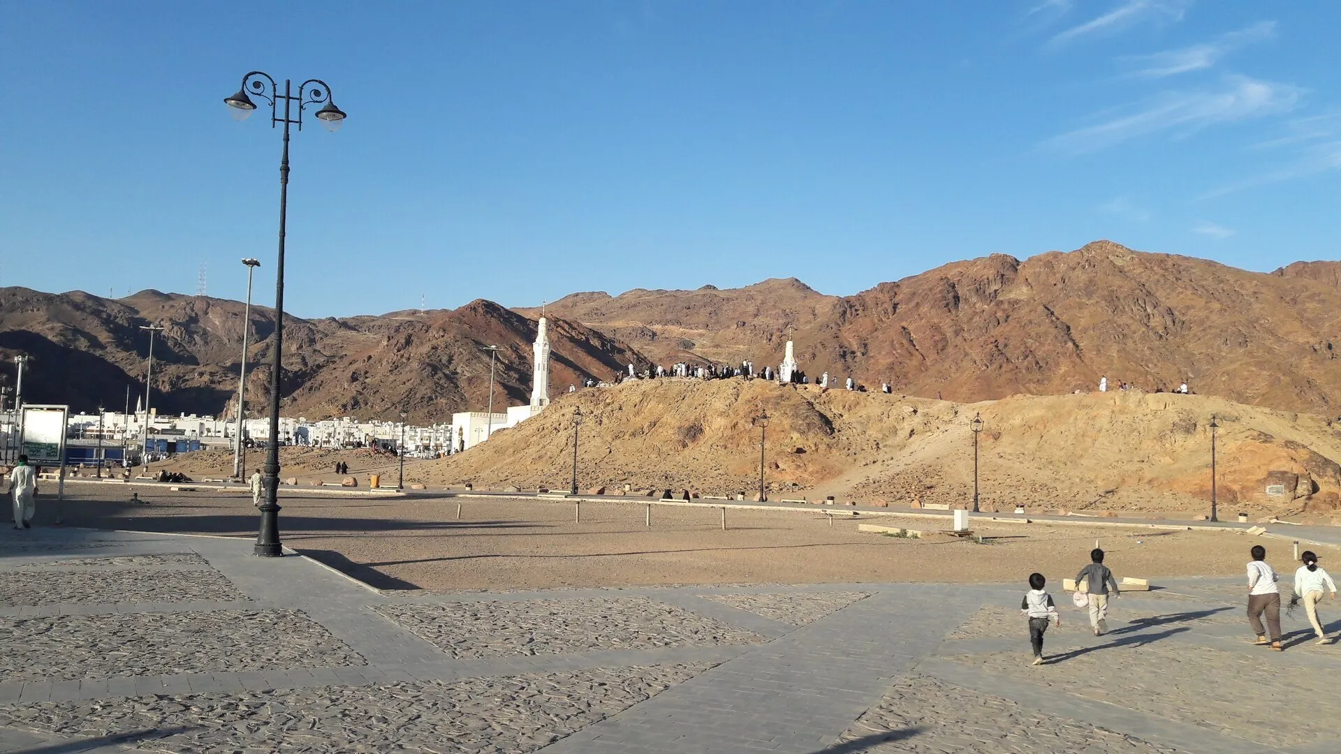 Colina dos Arqueiros diante do maciço rochoso de Uhud, com postes e pequenos grupos de visitantes.