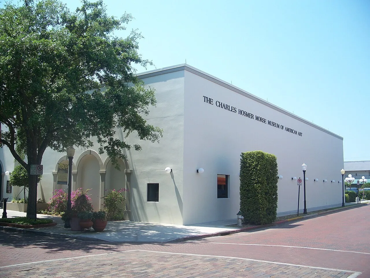 Fachada branca do Charles Hosmer Morse Museum, com nome na parede, árvores e rua de tijolos.