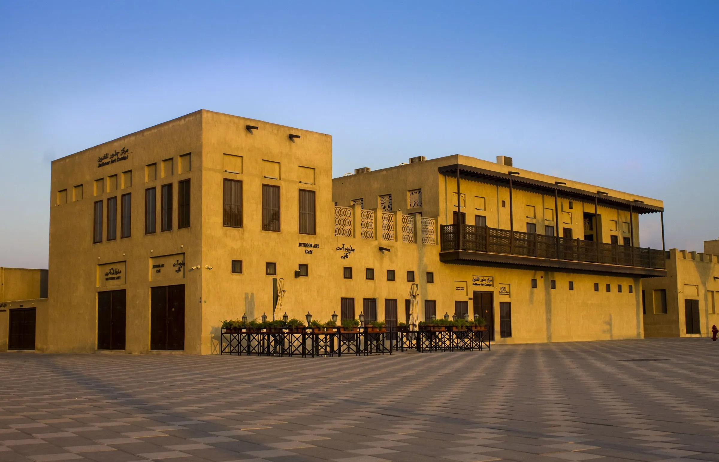 Restored historic houses in the Shindagha neighborhood, sand-toned in golden late-afternoon light, on an empty square.