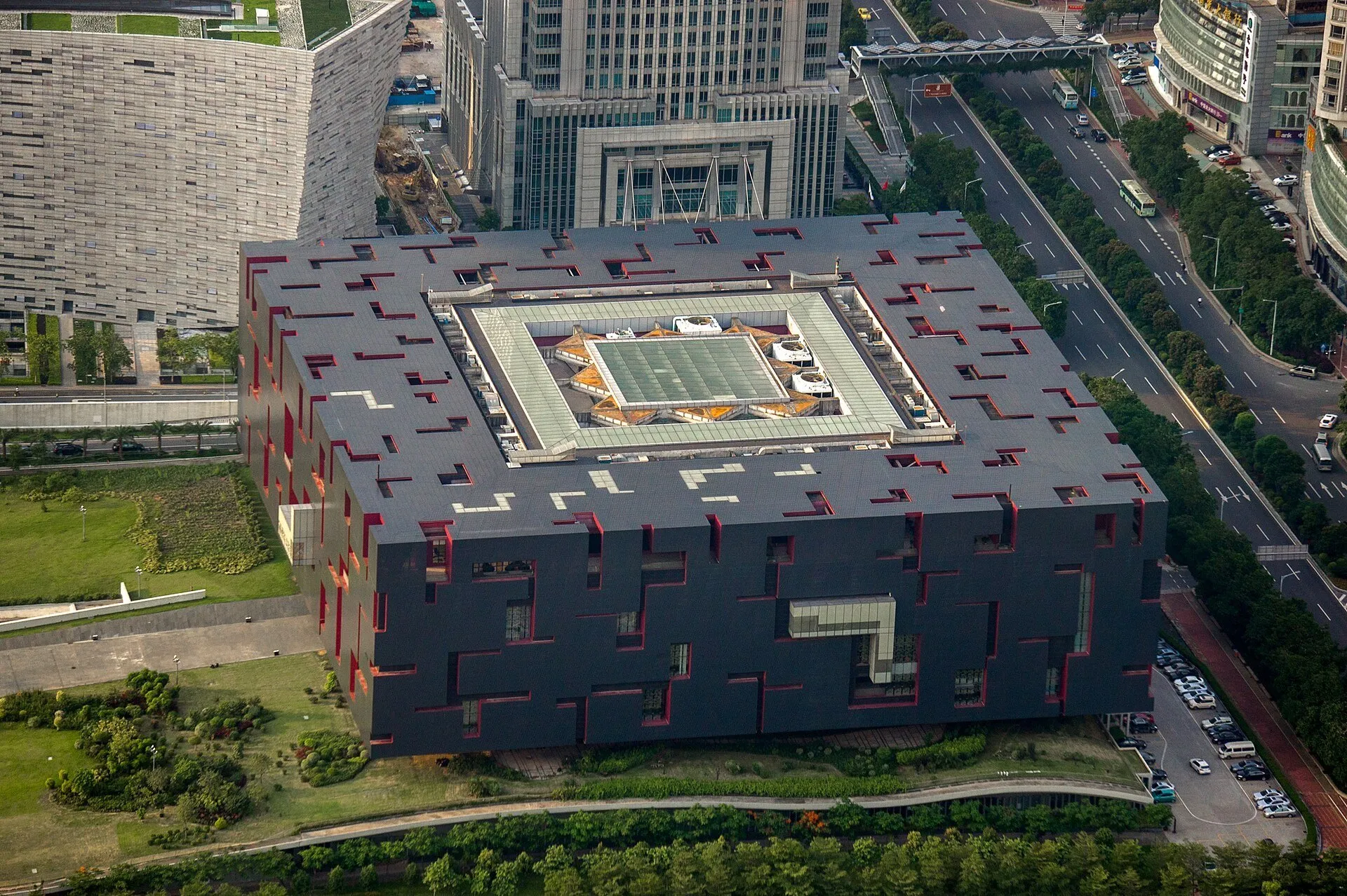 Vista elevada del Museo de Guangdong, con fachada gris, recortes rojos, patio central y calles alrededor.