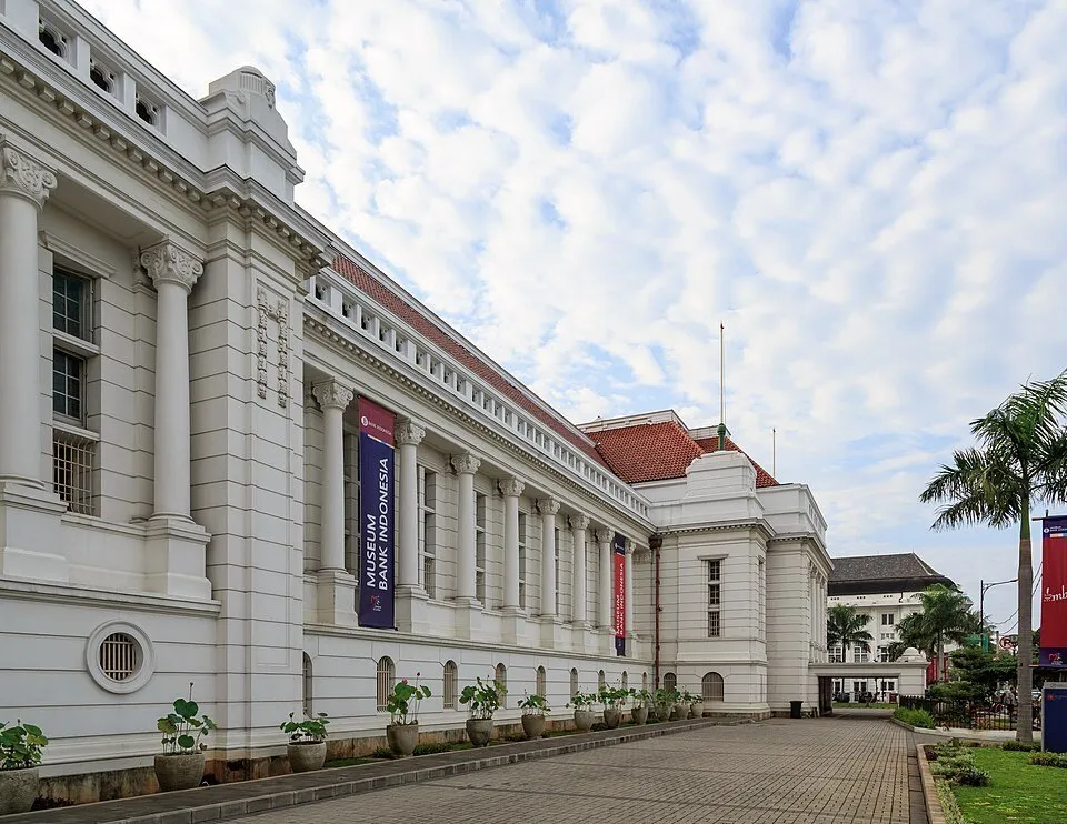 Fachada branca do Museu do Banco da Indonésia, com colunas, jardim e faixa com o nome da instituição.