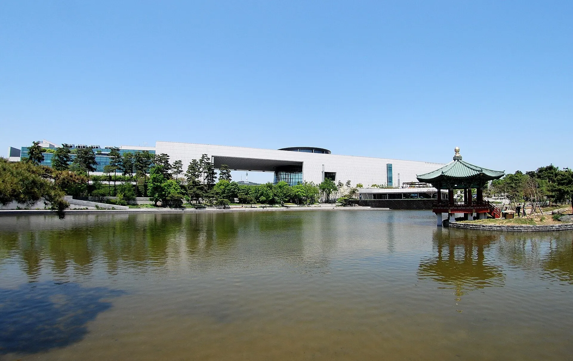 Museo Nacional de Corea junto a un estanque, con una abertura central en el edificio y un pabellón a la derecha.