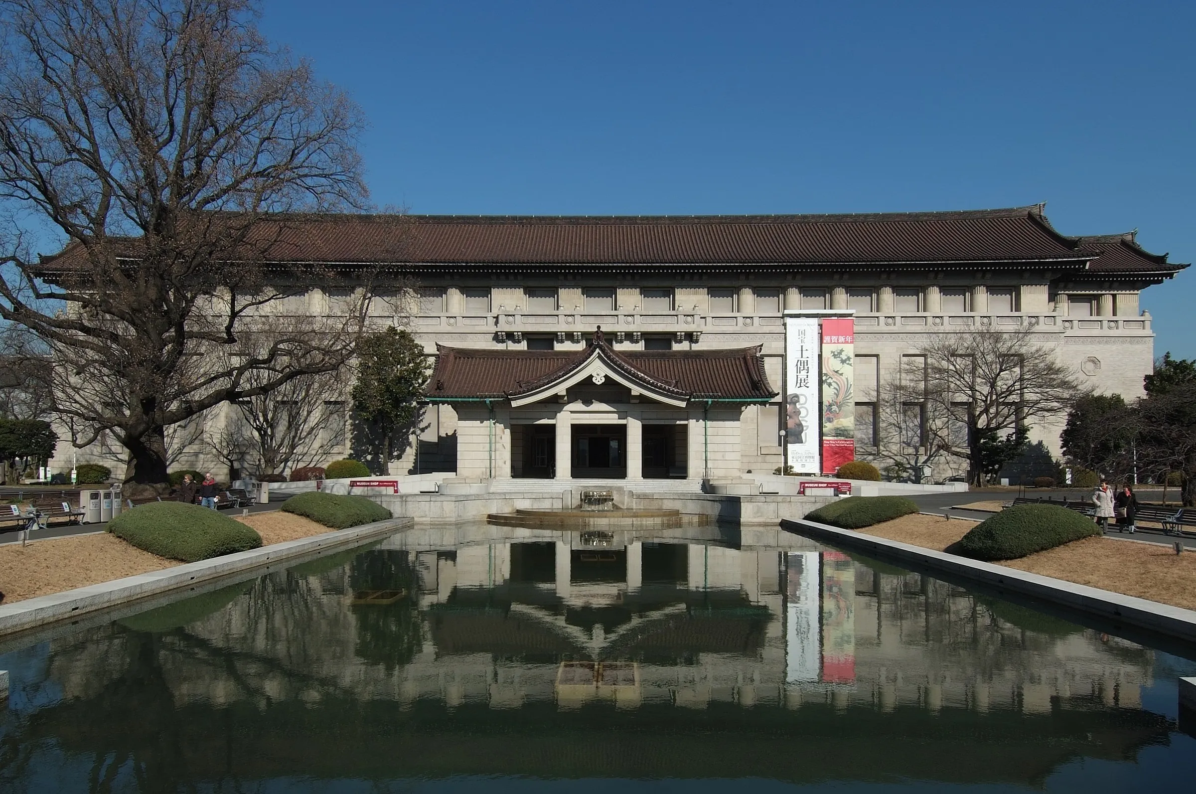 Fachada del Honkan del Museo Nacional de Tokio reflejada en el espejo de agua, bajo un cielo azul.