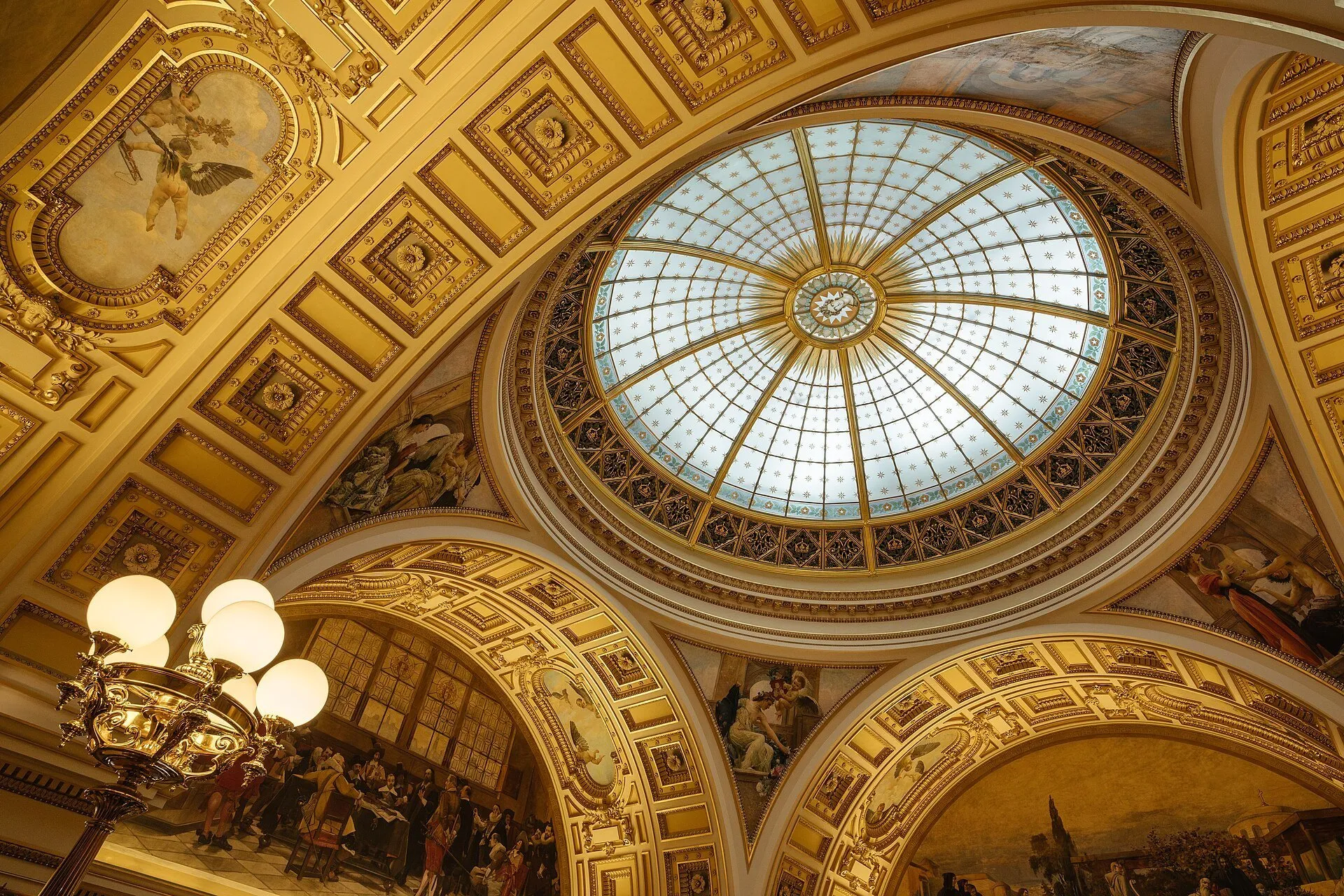 Cúpula acristalada del Museo Nacional de Praga, rodeada de pinturas, ornamentos dorados y una lámpara de araña.
