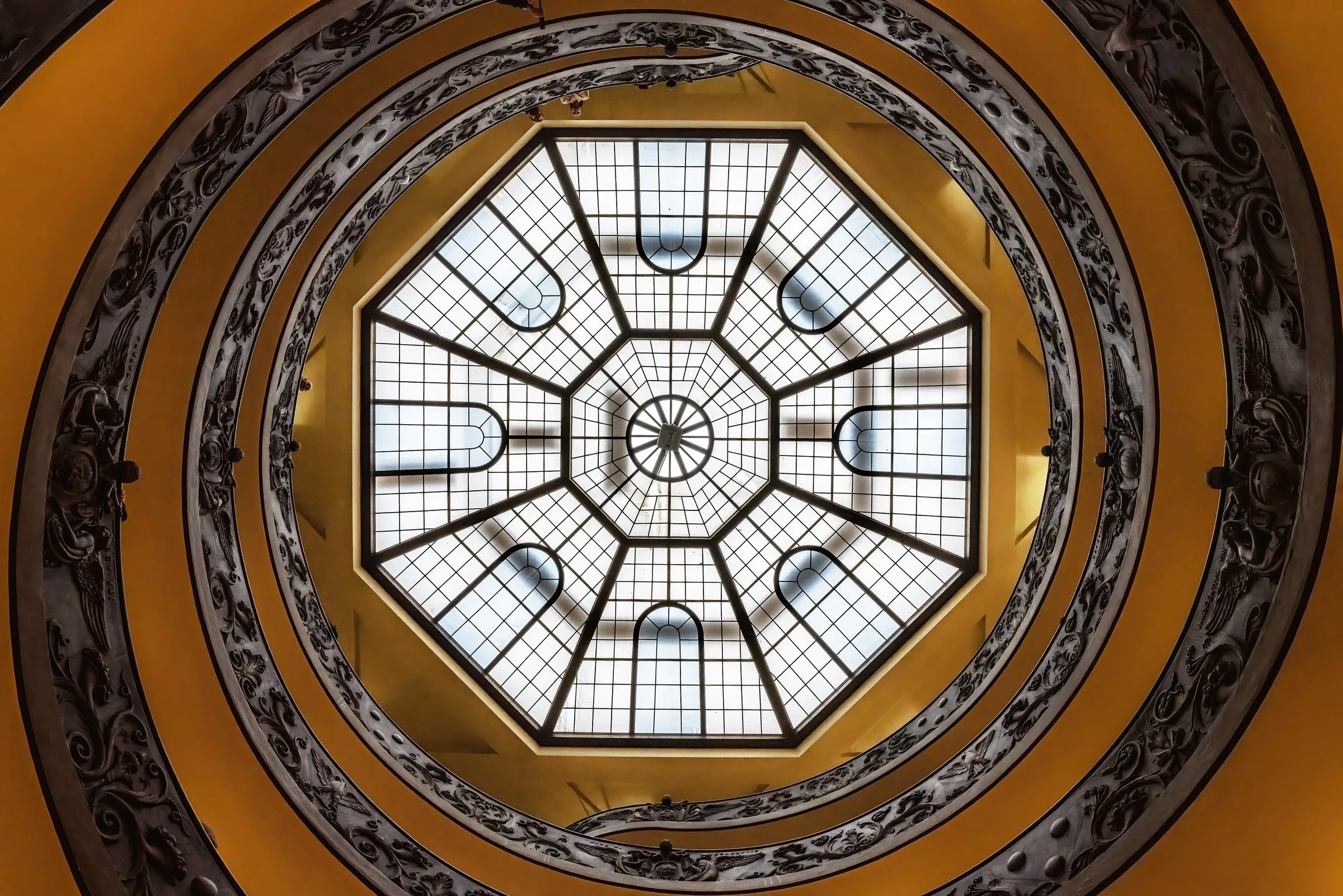 Spiral staircase of the Vatican Museums seen from below, with the octagonal skylight at the center and an ornate handrail.