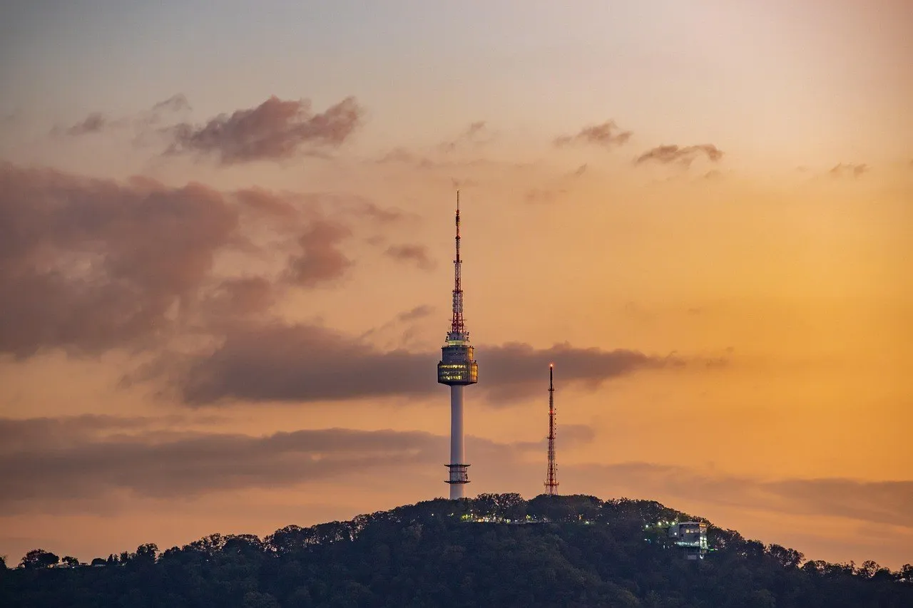 Torre N Seoul en el monte arbolado de Namsan, bajo un cielo anaranjado con nubes.