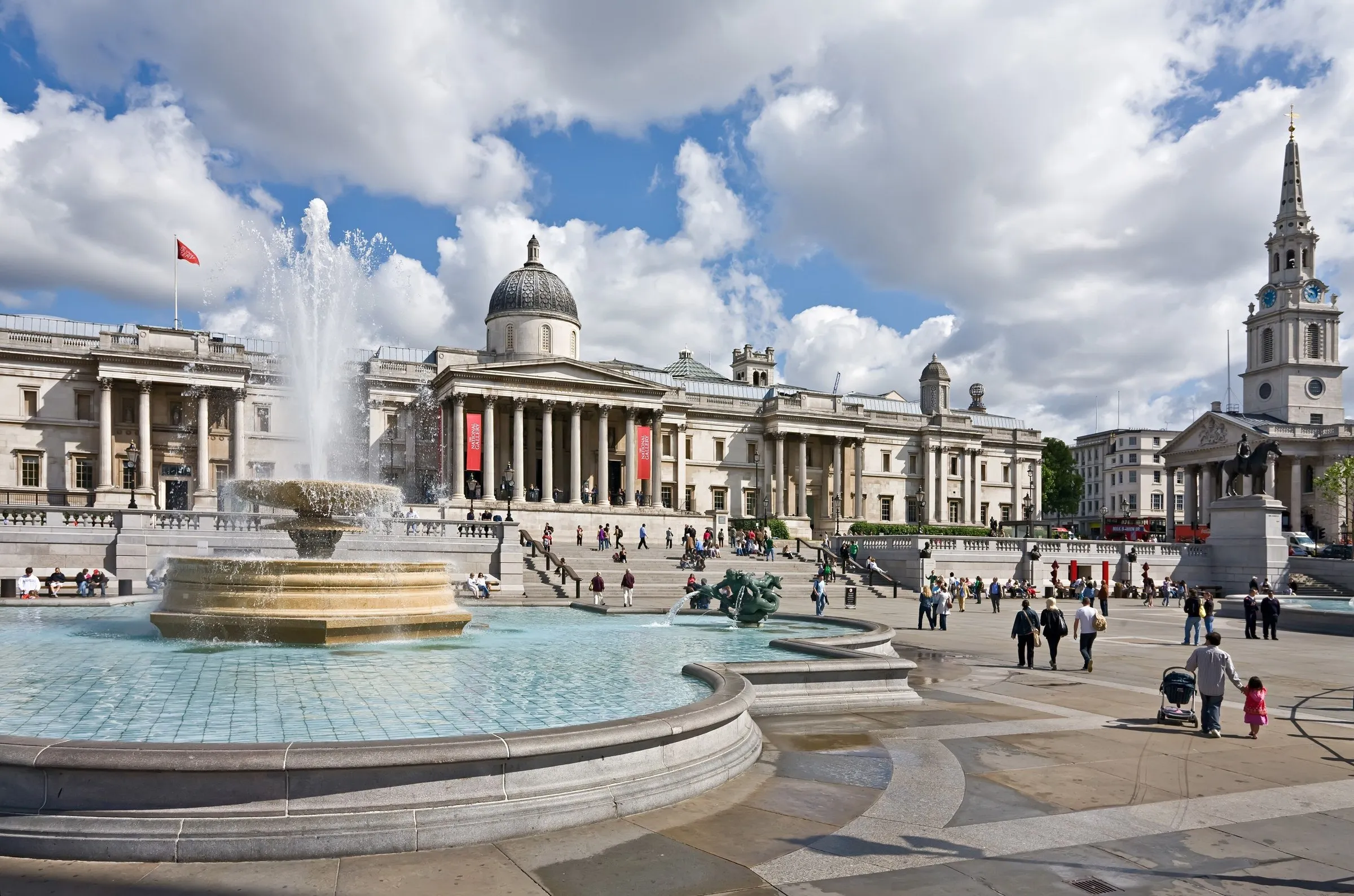 Columned facade of the National Gallery seen from Trafalgar Square, with a fountain in front and a church behind.