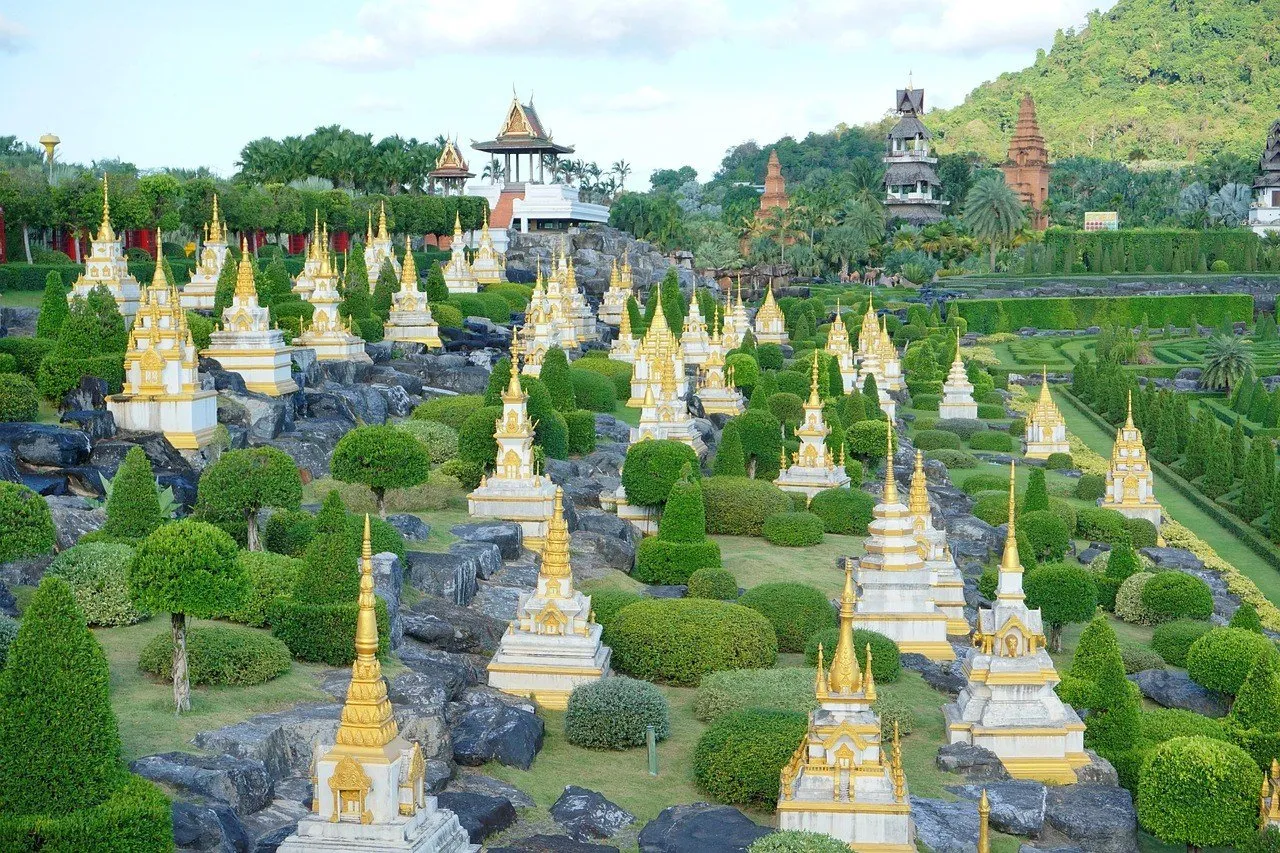 Jardim geométrico do Nong Nooch com arbustos aparados, pedras e pequenas torres brancas e douradas.