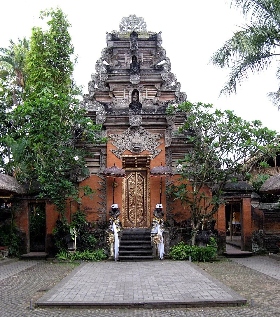 Portal esculpido del Palacio de Ubud con puerta dorada, dos guardianes y peldaños ante un patio.