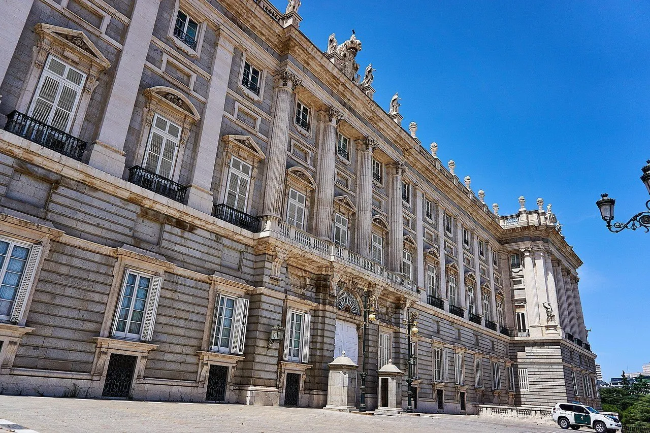 Stone facade of the Royal Palace of Madrid in perspective, with windows, statues and a blue sky.