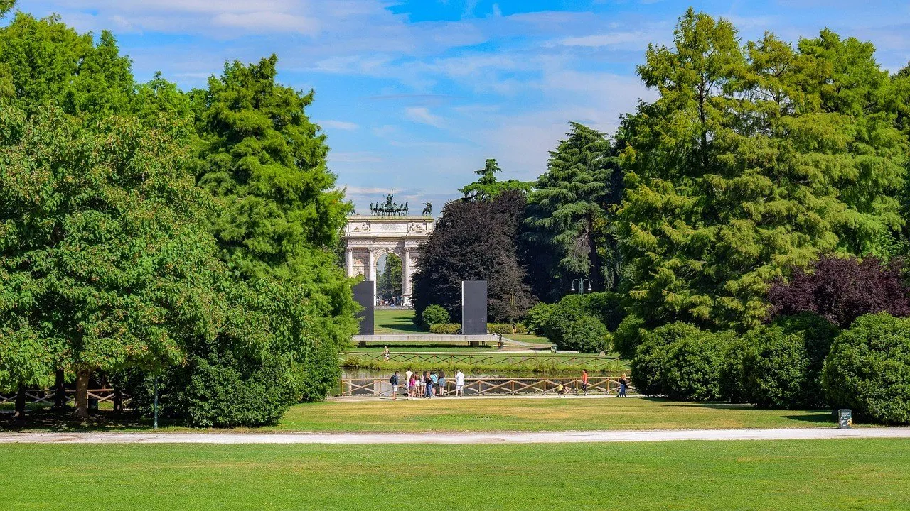 Lawns and trees of Parco Sempione, with small visitors and the Arco della Pace in the background.