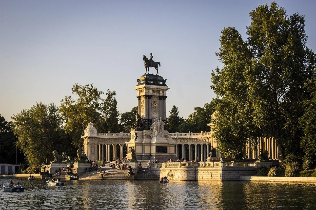 Monument to Alfonso XII beside the Retiro's Great Pond, with boats and trees in golden light.