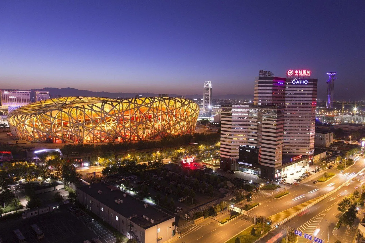 Estádio Ninho do Pássaro iluminado à noite, ao lado de edifícios e avenidas de Pequim.