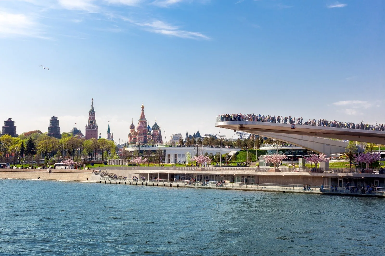 Puente mirador de Zaryadye sobre el río Moscova, con parque, árboles en flor y San Basilio al fondo.