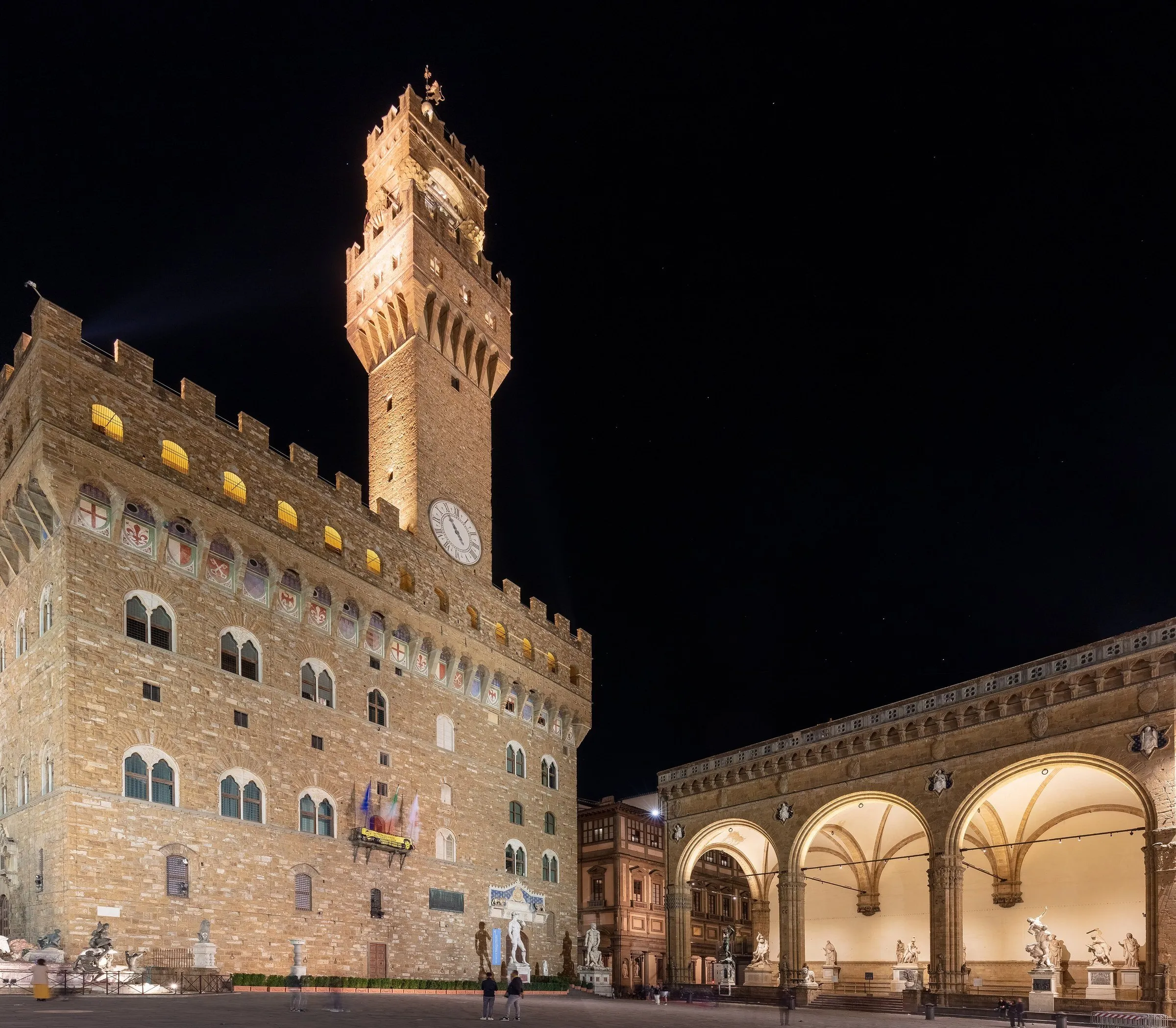 Palazzo Vecchio and sculptures of the Loggia dei Lanzi lit up at night in Piazza della Signoria.