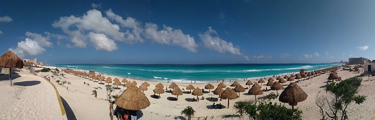 Vista panorâmica da Playa Delfines, com palapas de palha, areia clara e mar azul.