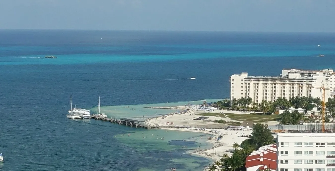Playa Langosta vista do alto, com areia, píer, embarcações, hotéis e mar azul.