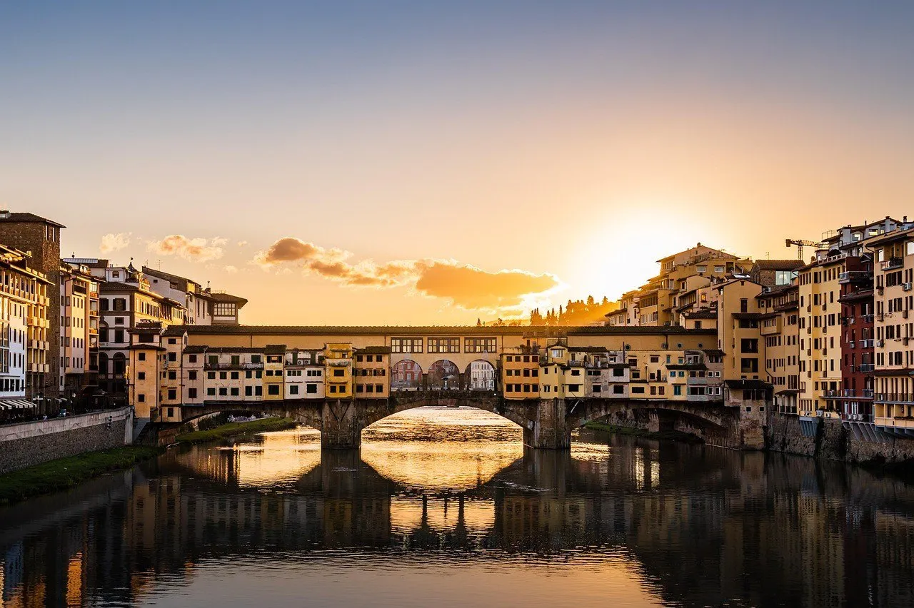 Front view of the Ponte Vecchio over the Arno, with golden sunset reflections between the arches.