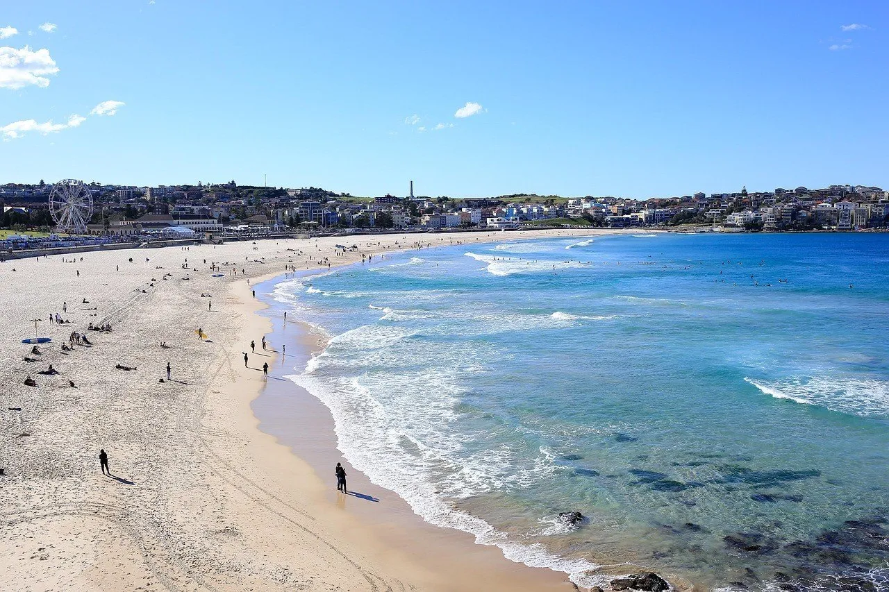 Curve of Bondi Beach, with pale sand, scattered swimmers, waves and buildings along the shore.