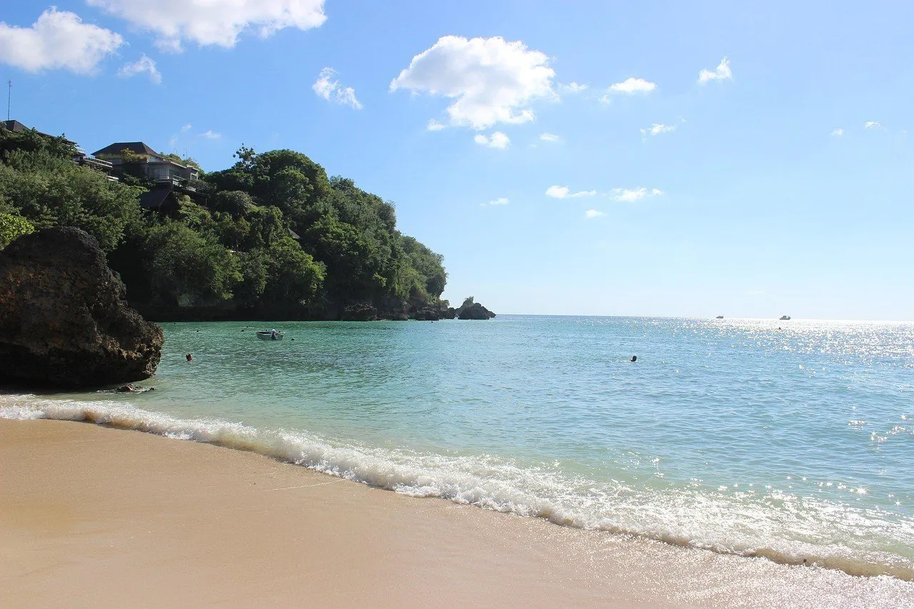 Arena clara y agua azul verdosa de la playa de Padang Padang, con rocas y vegetación en la orilla izquierda.
