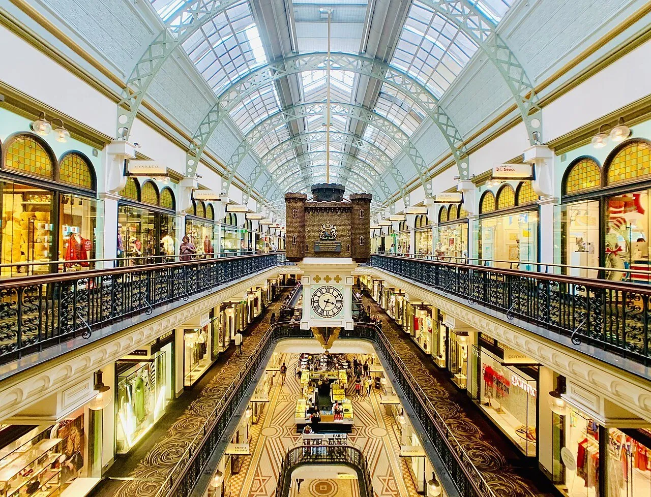 Interior galleries of the Queen Victoria Building, with a hanging clock, balustrades and a glass roof.
