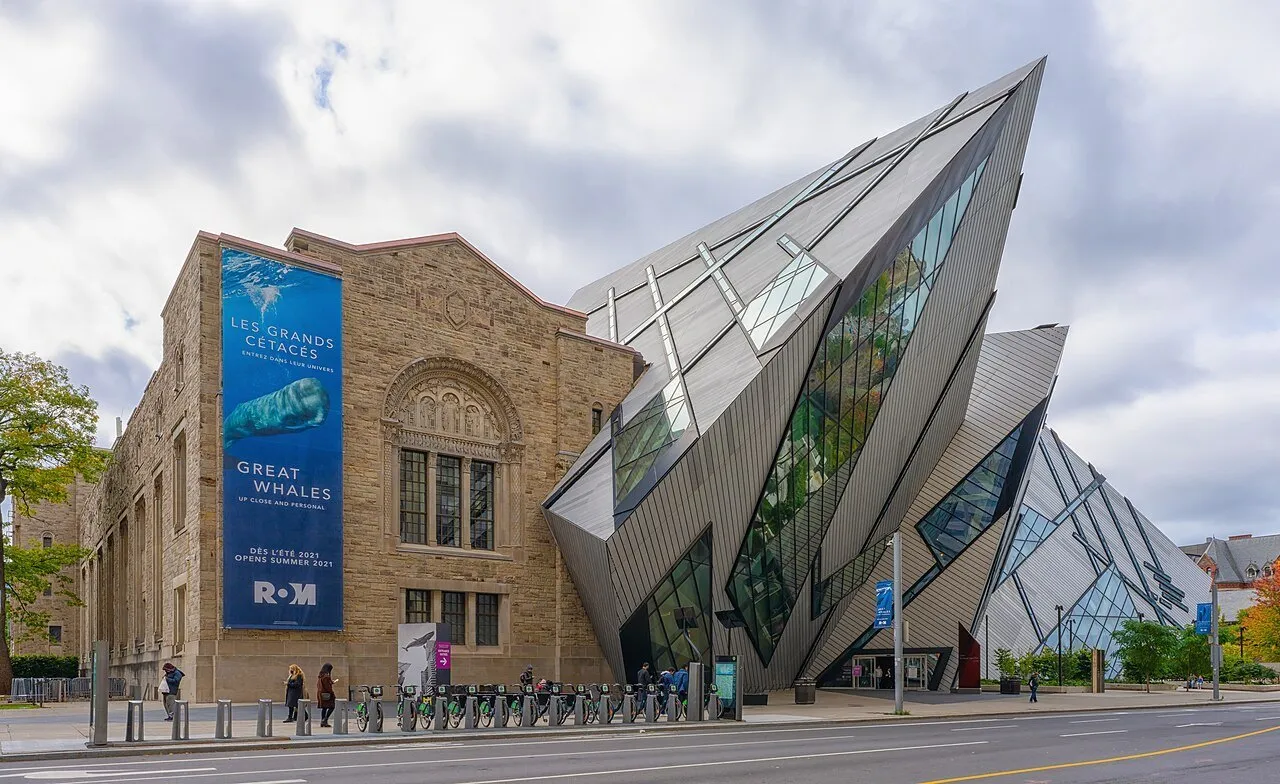 Fachada de pedra do Royal Ontario Museum junto ao volume angular de vidro e metal, com bicicletas na calçada.