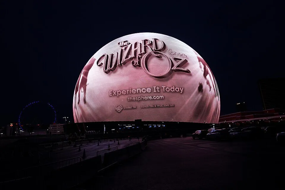 Sphere lit up with a The Wizard of Oz ad on its facade under a night sky, with an entrance area in front.