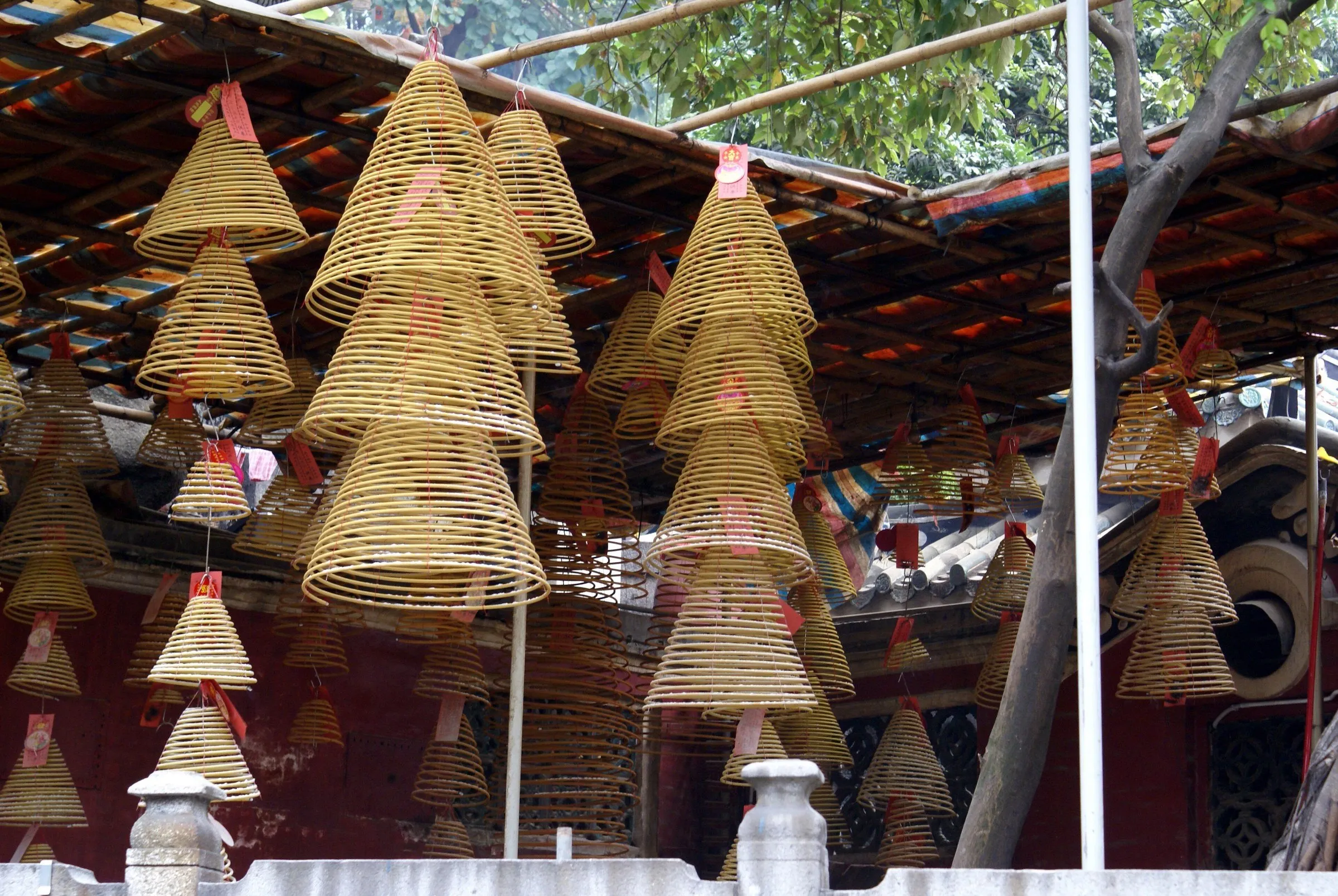 Decenas de espirales de incienso en forma de cono colgadas bajo un techo, con muros rojos del templo al fondo.