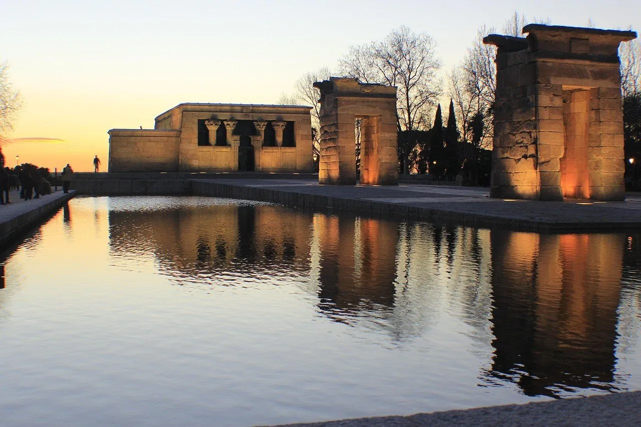 Temple of Debod and two stone gateways lit at dusk, reflected in the water.