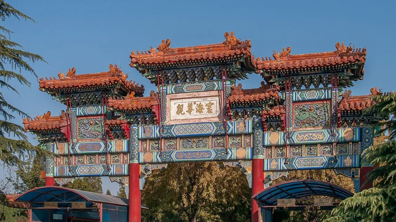Portal ornamentado do templo Yonghe, com colunas vermelhas e telhados decorados sob céu azul.