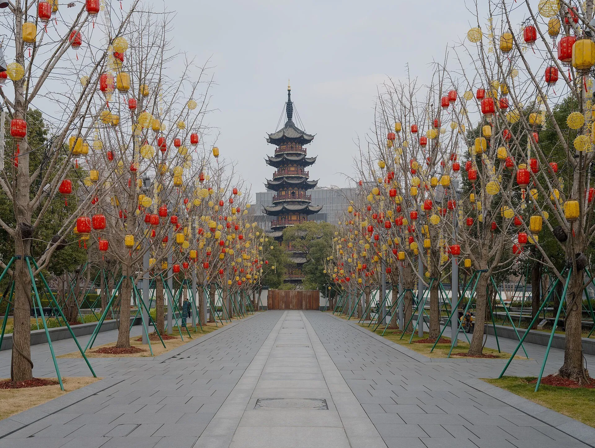Longhua Pagoda at the end of a path lined with trees and red and yellow lanterns.