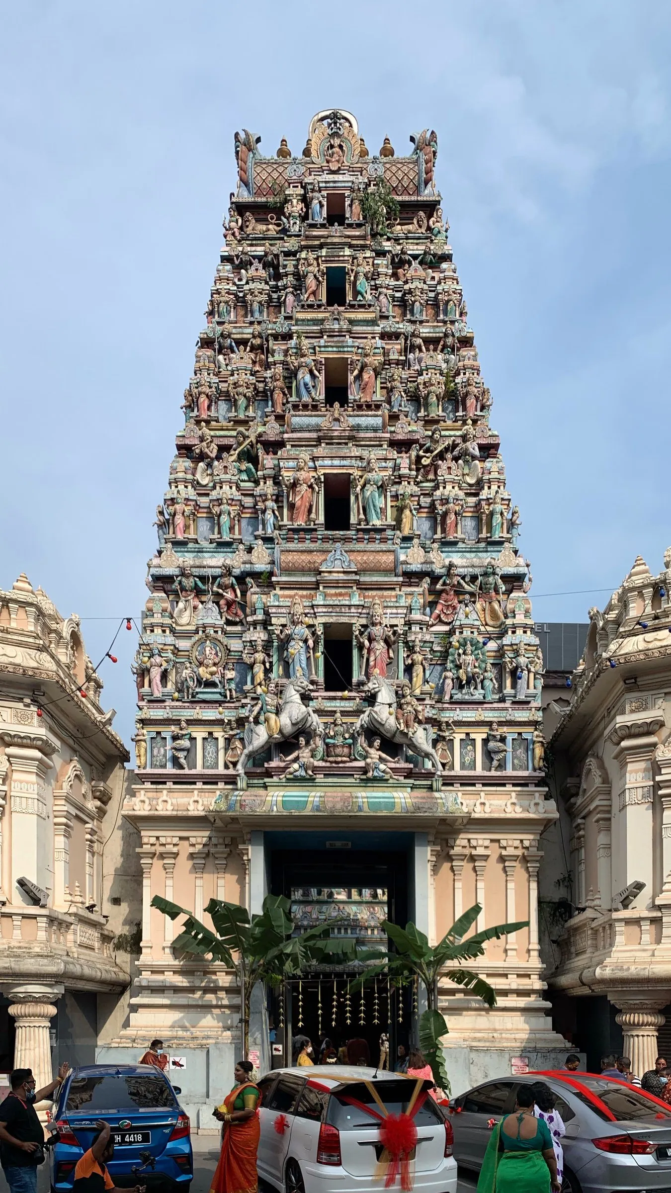 Torre gopuram colorida, coberta de esculturas de divindades, sobre a entrada de um templo hindu, sob céu azul.