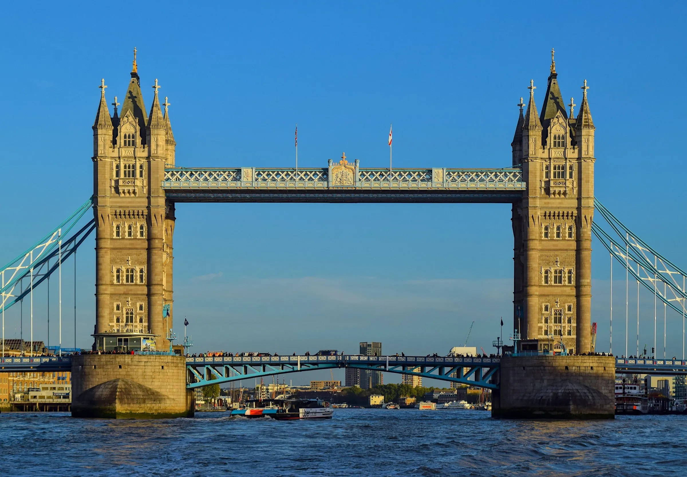Tower Bridge seen head-on over the Thames, with its two stone towers and a clear blue sky behind.