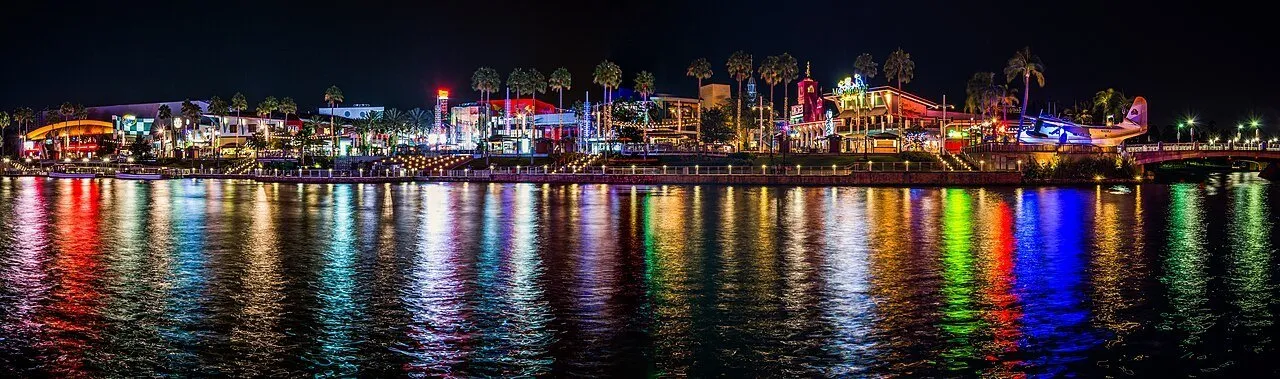 Panorama noturno das fachadas do Universal CityWalk Orlando com reflexos coloridos na água.