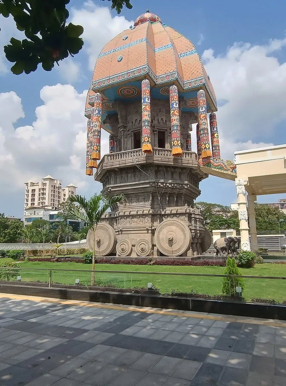 Carro processional de pedra do Valluvar Kottam, com rodas esculpidas, cobertura colorida e jardim.