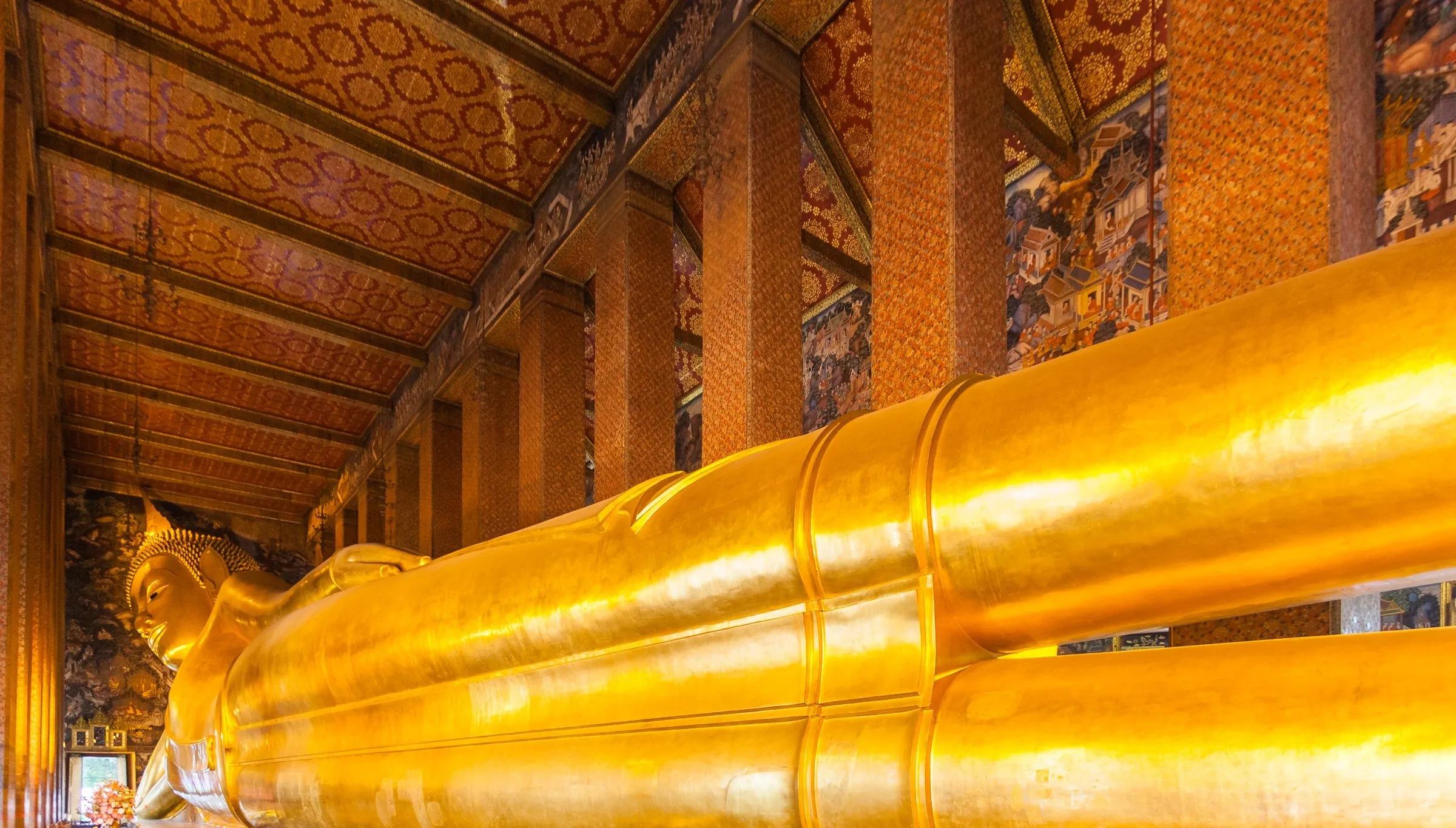 Estátua dourada do Buda Reclinado no Wat Pho, em Bangkok, vista em perspectiva ao longo do corpo, dentro do templo.