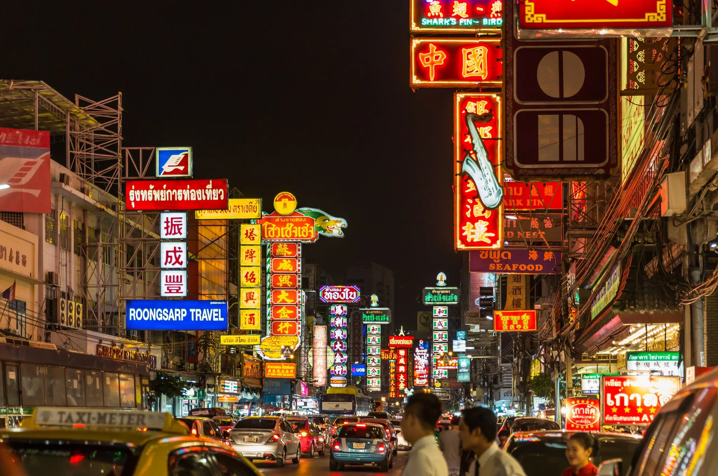 Rua Yaowarat, em Bangkok, à noite, com placas de neon em chinês e tailandês, táxis e pedestres.