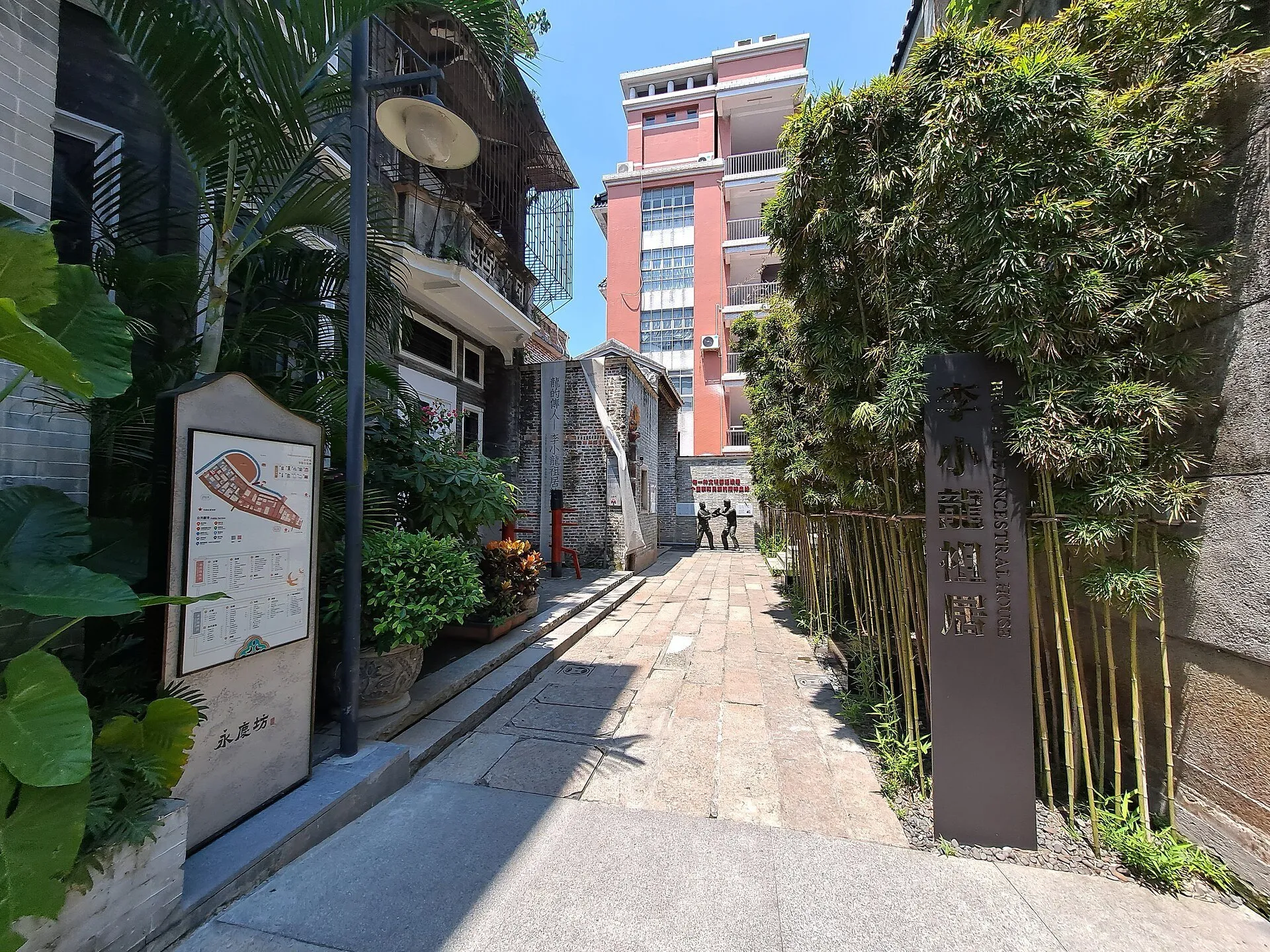 Callejón de Yongqing Fang con casas, bambúes, letreros y una fachada rosada al fondo.
